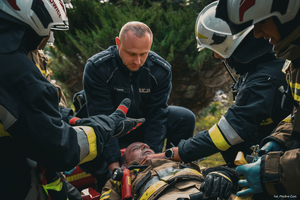 umundurowany policjant i strażacy udzielają pomocy strażakowi
