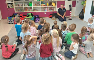 umundurowany policjant przed nim siedzące dzieci w sali przedszkolnej