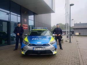 umundurowani policjanci stoją obok oznakowanego radiowozu przed budynkiem komendy