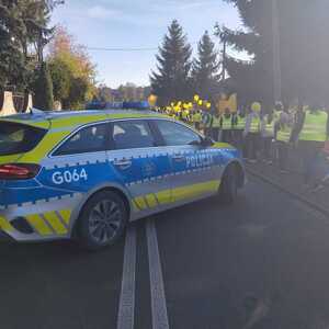 oznakowany radiowóz obok dzieci idące w kamizelkach odblaskowych