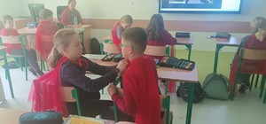 dzieci w szkolnych ławkach ubrane w czerwone peleryny