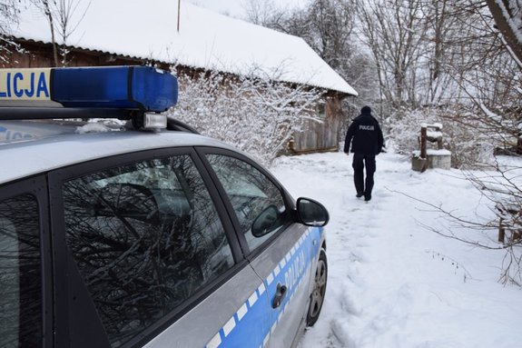 umundurowany policjant idzie po śniegu obok oznakowany radiowóz