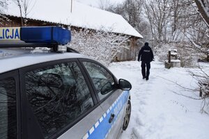 umundurowany policjant idzie po śniegu obok oznakowany radiowóz