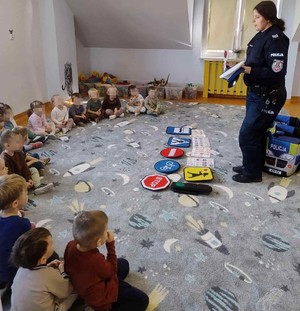 umundurowana policjantka na sali przed nią zabawkowe znaki drogowe i dzieci siedzące po turecku