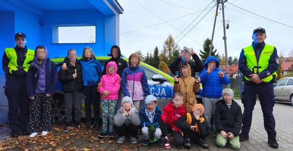 umundurowani policjanci wraz z dziećmi za nimi oznakowany radiowóz