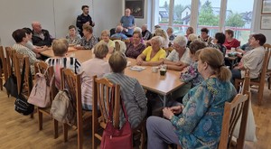 sala na której przy stole siedzą seniorzy umundurowany policjant przed ekranem z prezentacja