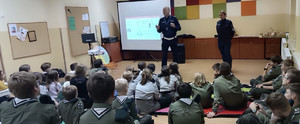 umundurowani policjanci na sali z harcerzami za nimi ekran z prezentacją