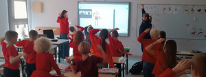 dzieci ubrane na czerwono na sali przed nimi umundurowana policjantka