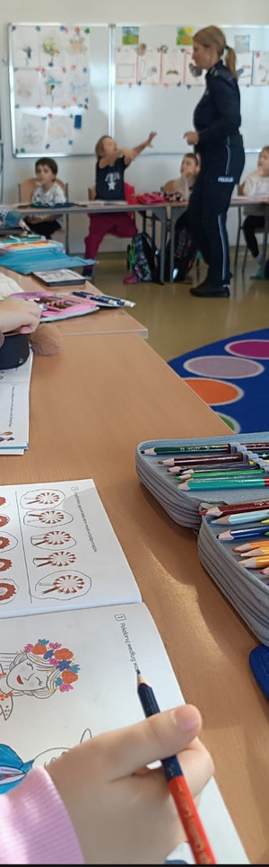 umundurowana policjantka obok dzieci siedzące w ławkach