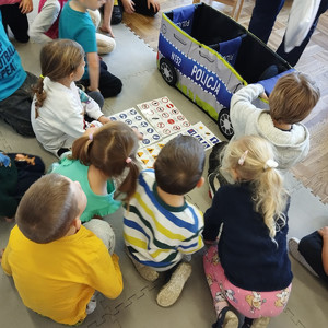 dzieci siedzące na podłodze obok nich radiowóz zabawka i znaki drogowe na kartkach papieru