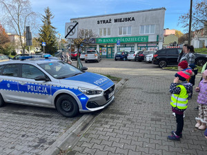 oznakowany radiowóz zaparkowany przed budynkiem obok dzieci