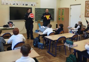 umundurowani policjanci trzymają znaki drogowe przed nimi siedzą w ławkach uczniowie