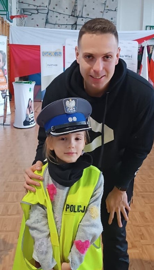 mężczyzna obok dziecko ubrane w kamizelkę odblaskową i czapkę policyjną