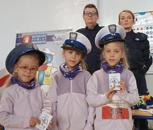 umundurowani policjanci obok dzieci ubrane w czapki policyjne