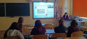 na sali uczniowie siedzą w ławkach przed nimi ekran z prezentacja