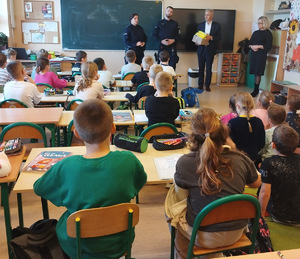 sala lekcyjna dwóch umundurowanych policjantów mężczyzna z pudełkiem z elementami odblaskowymi obok niego kobieta