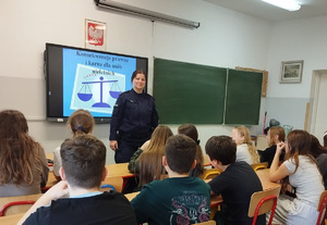 umundurowana policjantka za nią ekran z prezentacją dzieci siedzą w szkolnych ławkach