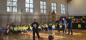 sala gimnastyczna dzieci w kamizelkach czterech umundurowanych policjantów na środku sali