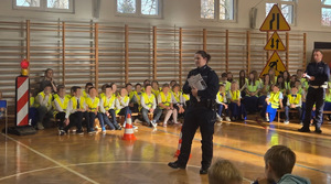 sala gimnastyczna na niej dzieci w kamizelkach i umundurowani policjanci