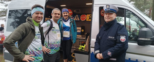 umundurowany policjant ruchu drogowego z biegaczami za nimi radiowóz