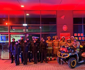 umundurowani funkcjonariusze przed podświetlonym budynkiem komendy