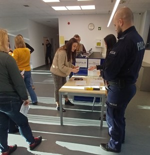 umundurowany policjant obok niego stół przed nim osoby