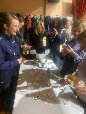 umundurowana policjantka przy stoliku edukacyjnym obok niej stoją kobiety