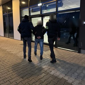 dwóch nieumundurowanych policjantów z opaską Policja prowadzi osobę do budynku Komendy