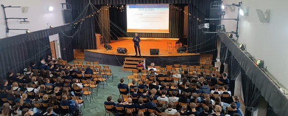 aula wypełniona uczniami na podeście umundurowana policjantka z mikrofonem