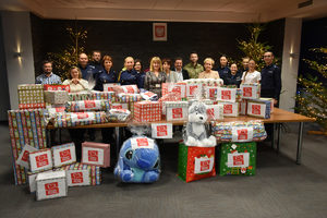 policjanci i pracownicy na grupowym zdjęciu przed nimi na stołach zapakowane prezenty