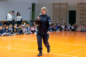 umundurowana policjantka z mikrofonem na sali podczas prelekcji wokół siedzą dzieci