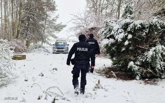 umundurowani policjanci idą drogą leśną zimą w tle radiowóz