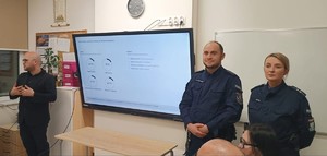 umundurowana policjantka i policjant obok mężczyzna stoją pod tablicą w klasie podczas spotkania z rodzicami