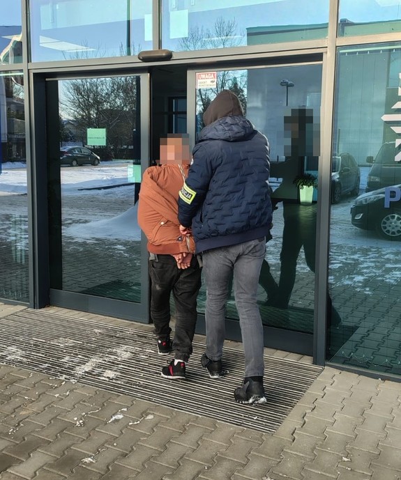 nieumundurowany policjant prowadzi zatrzymanego do budynku komendy