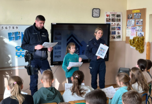 umundurowani policjnci z nimi dziewczynka stoją przed siedzącymi uczniami
