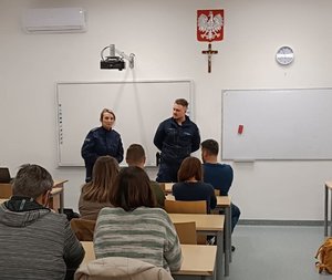 umundurowana policjantka i policjant stoją w sali lekcyjnej przed nimi siedzą w ławkach rodzice dzieci