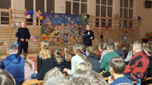 umundurowani policjanci przed nimi siedzą uczniowie w sali