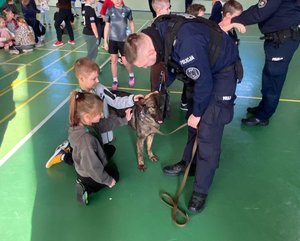 policjant w mundurze z psem służbowym którego głaskają dzieci