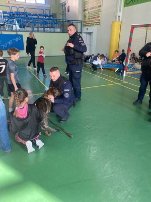 policjanci w mundurach z nimi pies służbowy przed nimi stoją dzieci