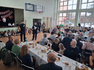 policjant i policjantka stoją na sali przed nimi siedzą seniorzy