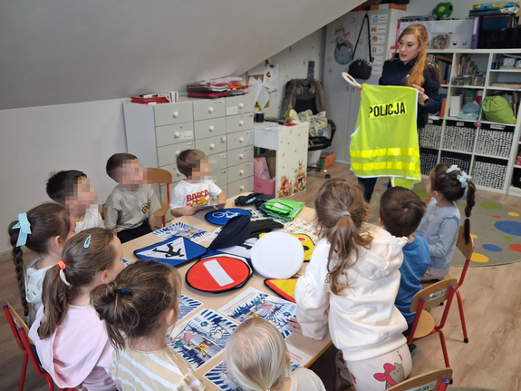 policjantka w mundurze przed nią siedzą dzieci, pokazuje im policyjną kamizelkę