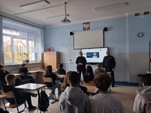 policjantka i policjant w sali przed nimi w ławkach siedzą uczniowie