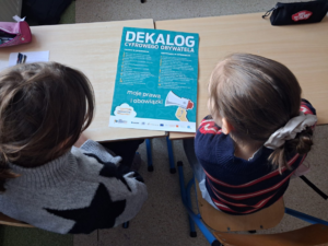 dzieci siedzące w ławce przed nimi ulotka edukacyjna