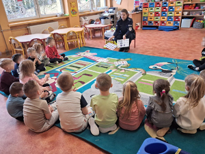 policjantka przed nią siedzą dzieci pokazuje im materiały edukacyjne
