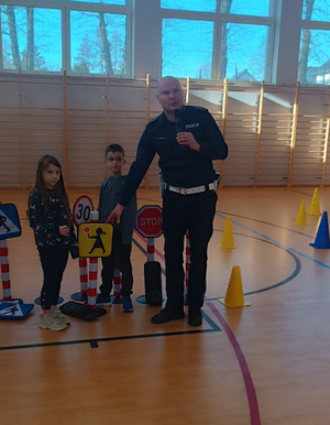 policjant w mundurze obok niego dzieci i znaki drogowe w sali gimnastycznej