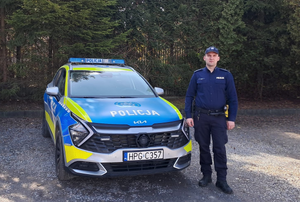 policjant w mundurze stoi obok oznakowanego radiowozu