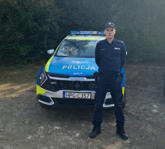 policjant w mundurze stoi przed oznakowanym radiowozem