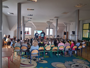 policjantka i policjant w mundurach przed nimi siedzą uczniowie na sali