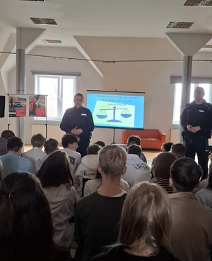 policjantka i policjant w mundurach przed nimi siedzą uczniowie podczas prelekcji