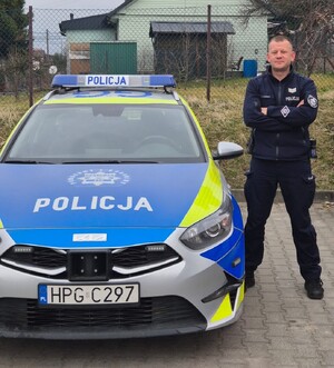 policjant w mundurze stoi obok oznakowanego radiowozu